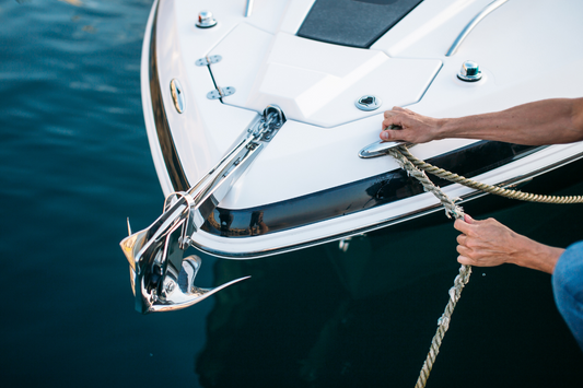 Front bow of a boat with a mounted stainless steel anchor and a man tying a rope around a bow cleat